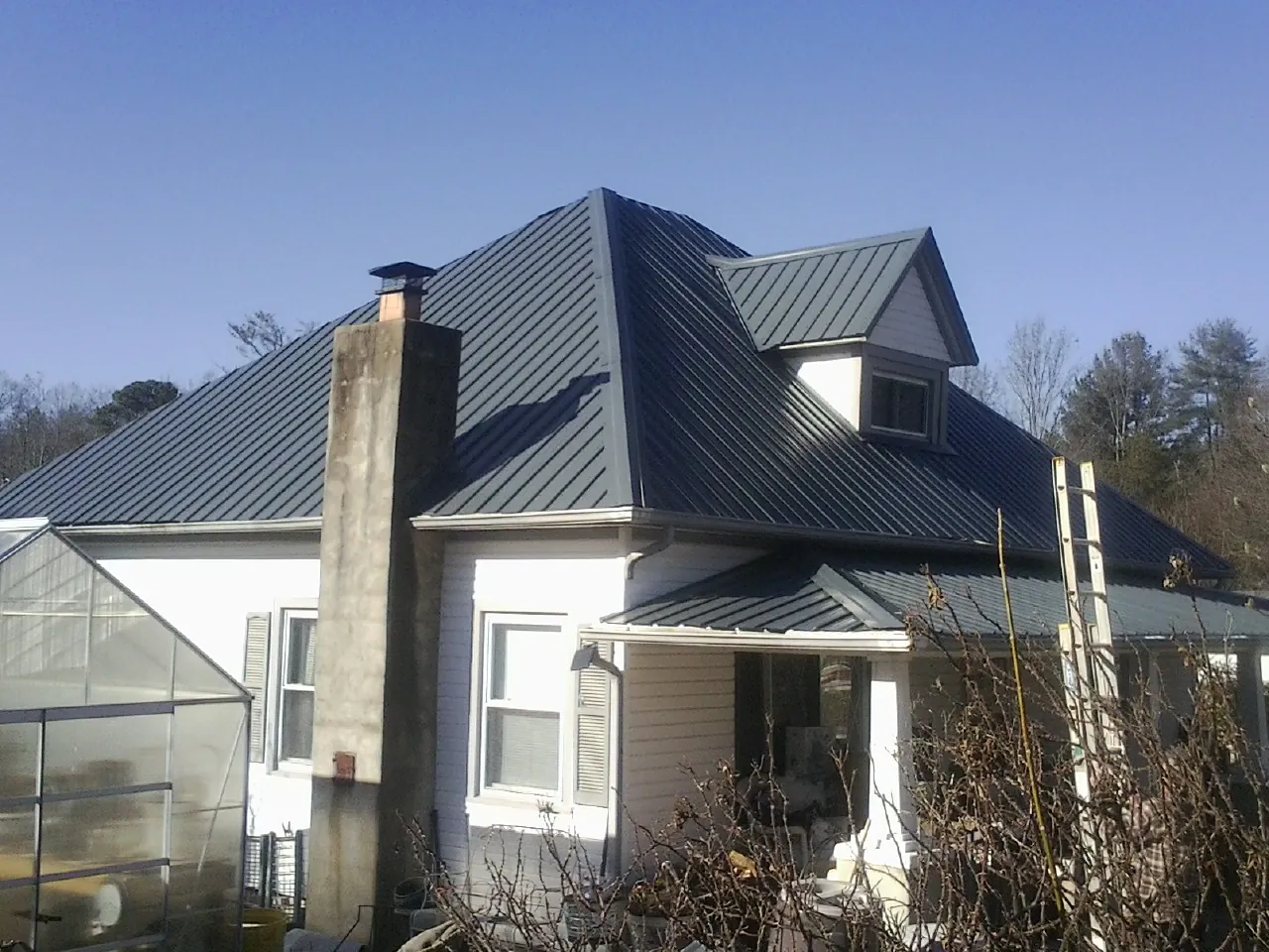 Dark blue standing seam metal roof on a white farmhouse with dormer — Slate & Tile Roof Repair by Roofing Brothers in Pemberville
