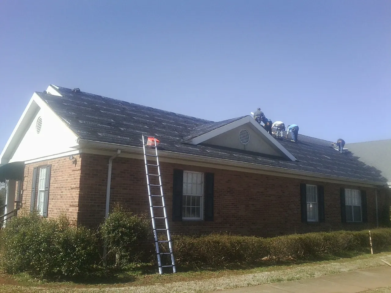 Crew tearing shingles off a brick ranch roof with a ladder set — Emergency Roof Repair work by our crew in Pemberville