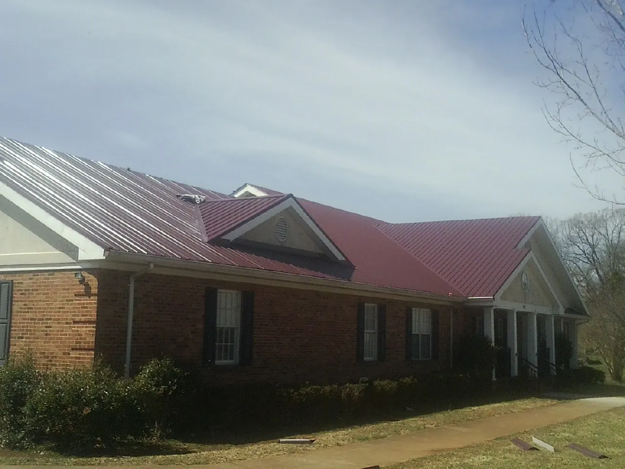 Red metal roof with gabled entries on a long brick building, from a Hail Damage Roof Repair job in Pemberville