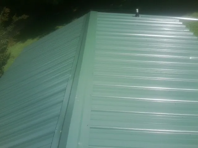 New green metal panels meeting at the ridge of a roof — Flat Roof Repair work by our crew in Pemberville