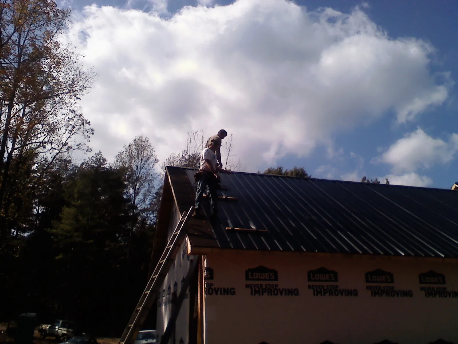 Roofer fastening dark metal panels high against a cloudy sky, from a Roof Inspection job in Pemberville