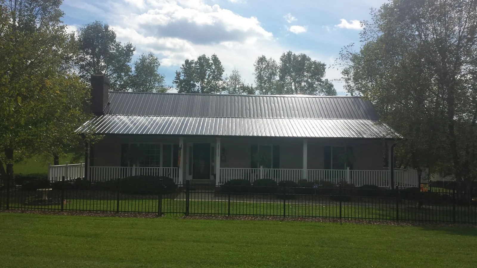 Gray metal roof on a brick ranch with a full width front porch — Gutter Guard Installation work by our crew in Pemberville