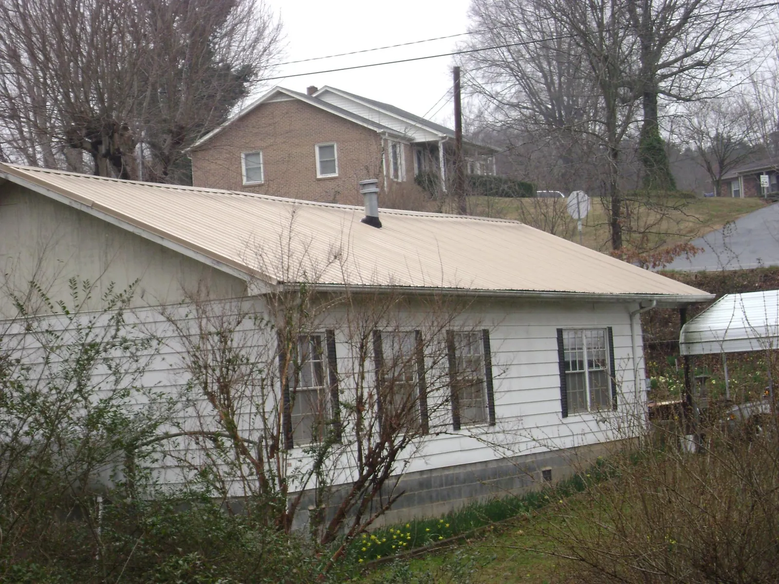 Tan metal roof on a white sided house set into a hillside — Commercial Roofing by Roofing Brothers in Pemberville