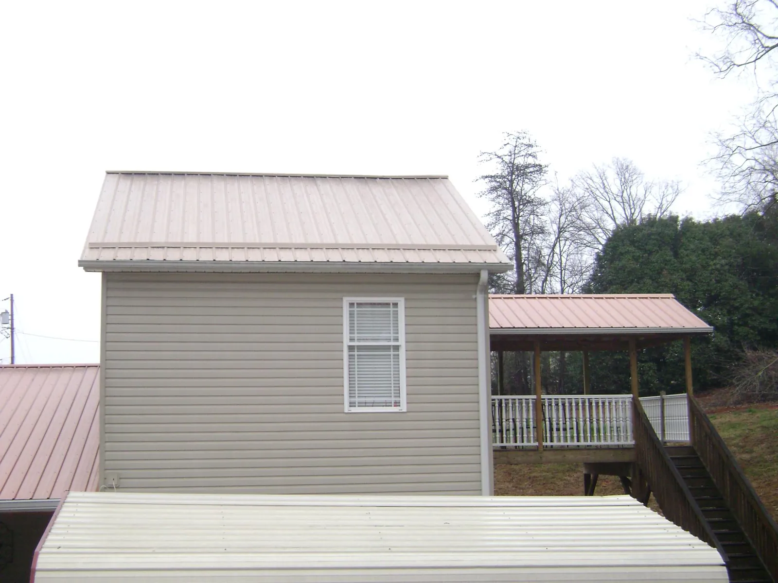 Tan metal roofs on a two story addition and attached porch, from a Roof Replacement job in Pemberville